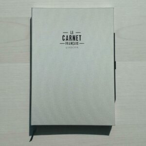 Carnet California gris métallisé vue de face avec couverture effet filet, logo Le Carnet Français en noir, marque-page intégré noir, fond minimaliste, lumière douce, texture métallique et tactile visible.