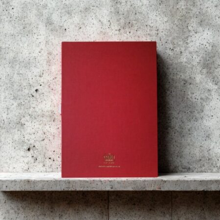 Dos d'un carnet rouge corail posé sur béton, avec la mention dorée "Le Carnet Français".