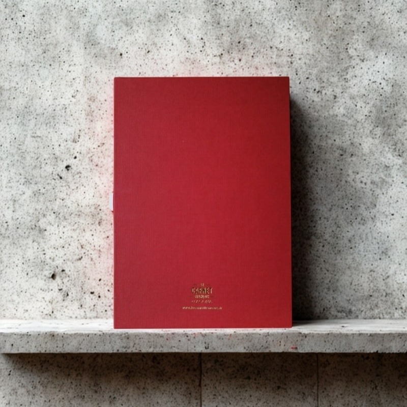 Dos d'un carnet rouge corail posé sur béton, avec la mention dorée "Le Carnet Français".